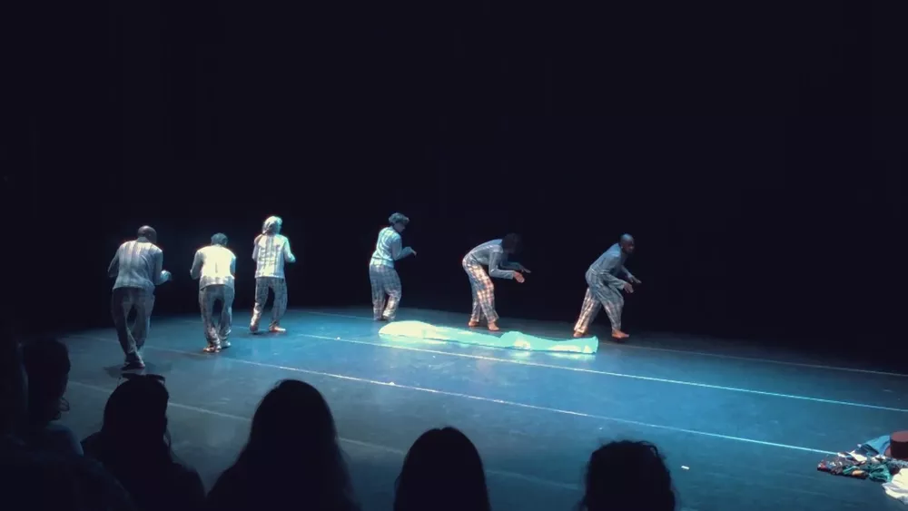 Six danseurs en pantalons à carreaux sur la scène bleutée de La Barque des 100 voix, public en silhouette