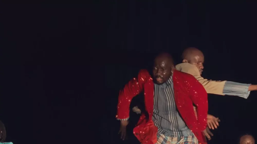 Plan serré d’un danseur en veste rouge pailletée, un partenaire bras tendu derrière lui