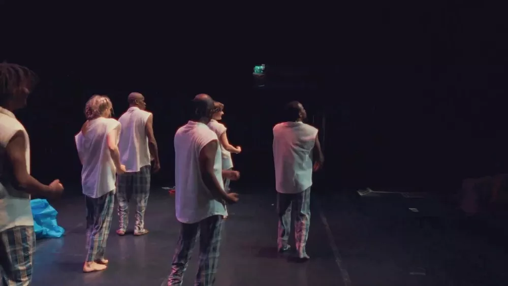 Danseurs en débardeurs blancs et pantalons à carreaux vus de dos sur la scène sombre
