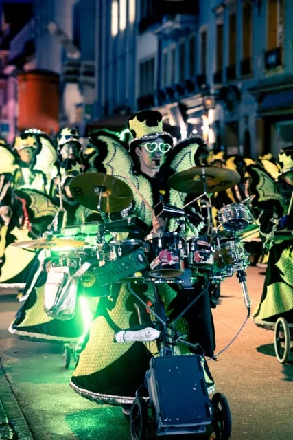 Batteur de guggenmusik en costume vert fluo sur une batterie roulante, cortège de nuit des Brandons d'Yverdon